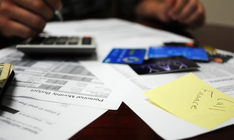 desk full of paperwork, credit cards, and a person using a calculator