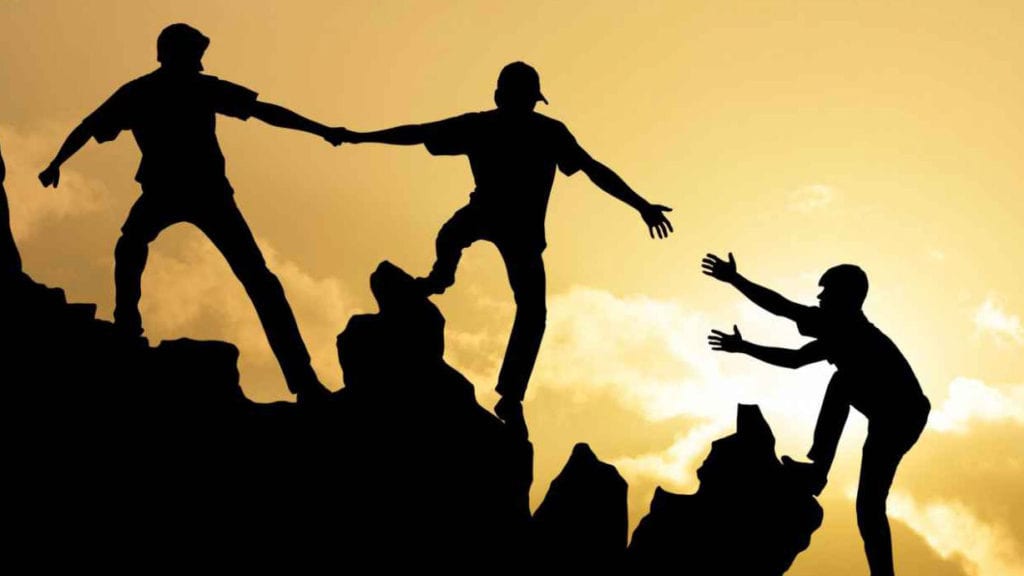 silhouettes of men helping each other climb a mountain