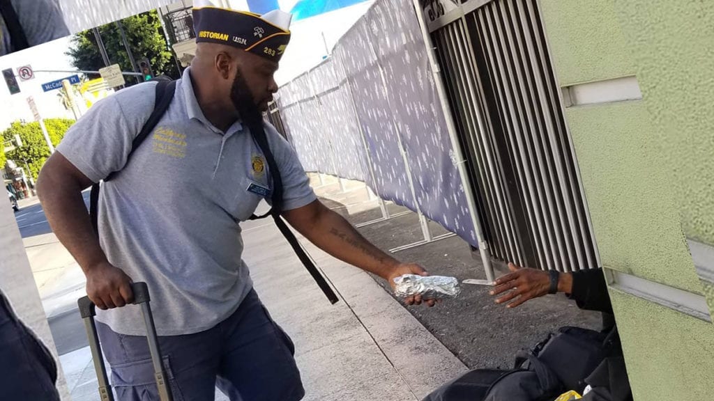 Ronald Reagan-Palisades Post 283 member Andre Andrews hands a burrito to a person sitting on an L.A. sidewalk