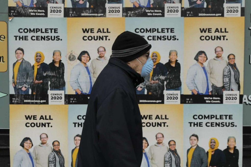 man with mask walks in front of Census posters