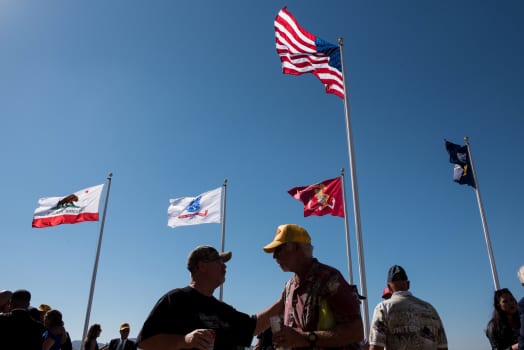 United States military veterans and guests gather in front of the flag poles
