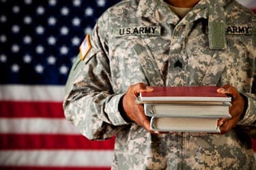 army soldier in uniform holding books in front of an american flag