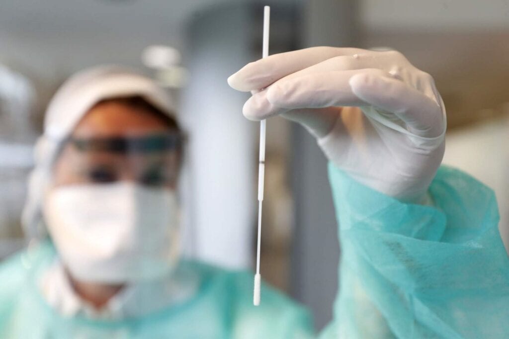 nurse in scrubs and a face mask holding a COVID-19 testing stick