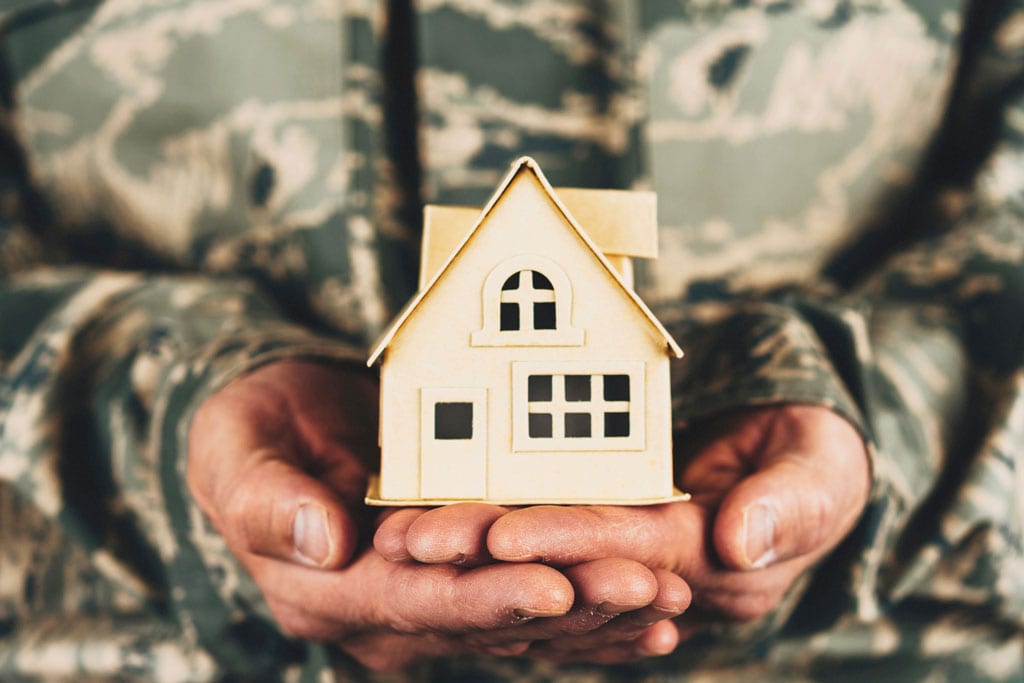 uniformed service member holding a model house in front of an american flag