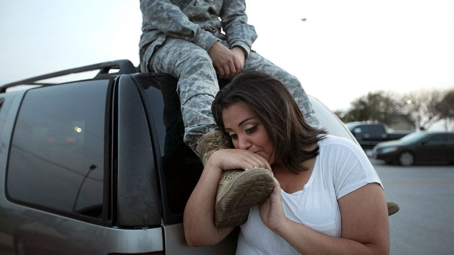 woman hugging the leg of veteran sitting on top of a car behind her
