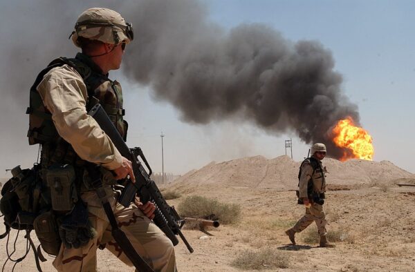U.S. soldiers advance during the 2003 invasion of Iraq. An oil field, lit by the Iraqi military, burns in the background.