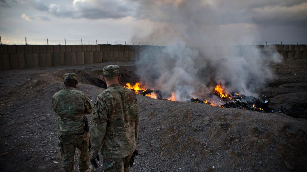 two servicemembers stand near a burn pit