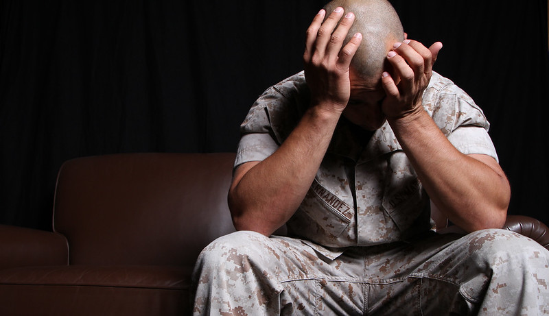 A U.S. Marine with his head in his hands, clearly distressed as he sits on a couch in a dark room