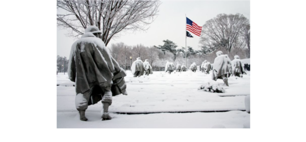snow covers the Korean War memorial in Washington DC while an American flag flies in the distance