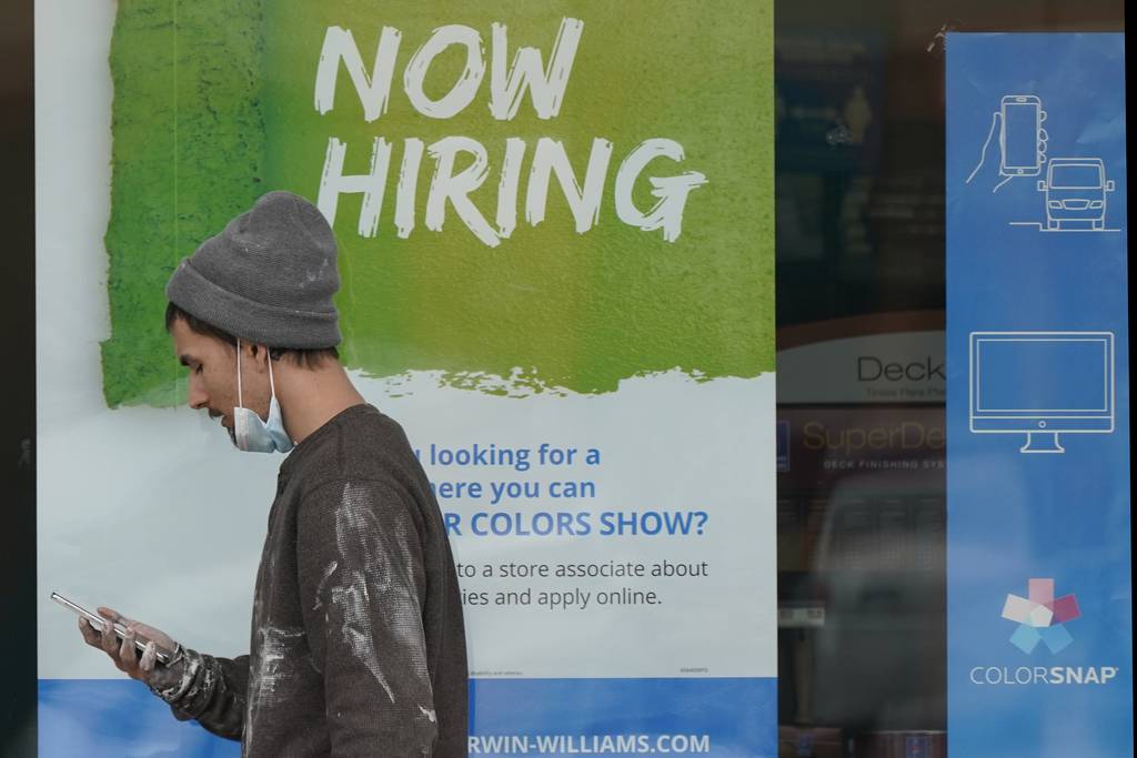 A man walks past a "Now Hiring" sign on a window