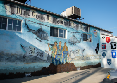 Mural on one of the outside walls of American Legion Post 139. Shows three men and two airplanes. States "Welcome Home Veterans" and "We left as strangers - came back as brothers"